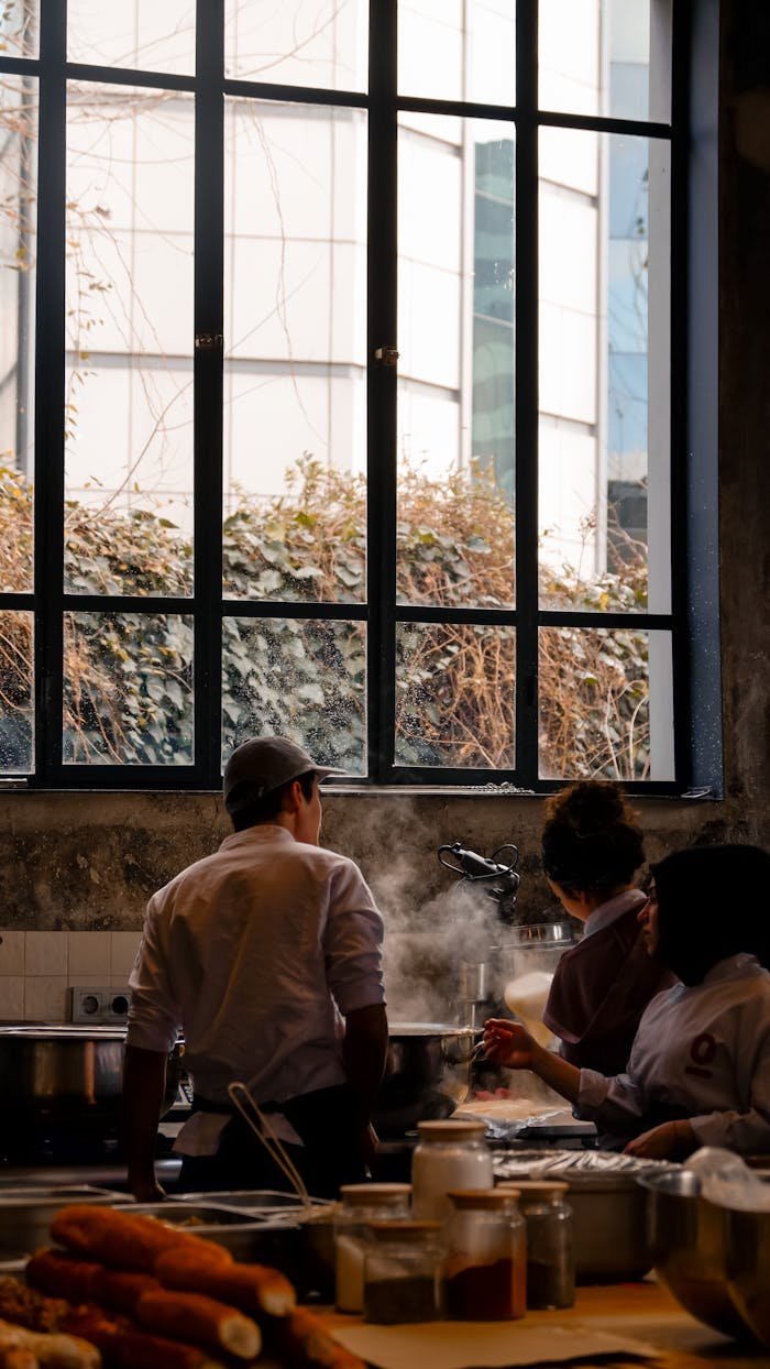 Professional chefs work together preparing meals in a restaurant kitchen with steam rising.