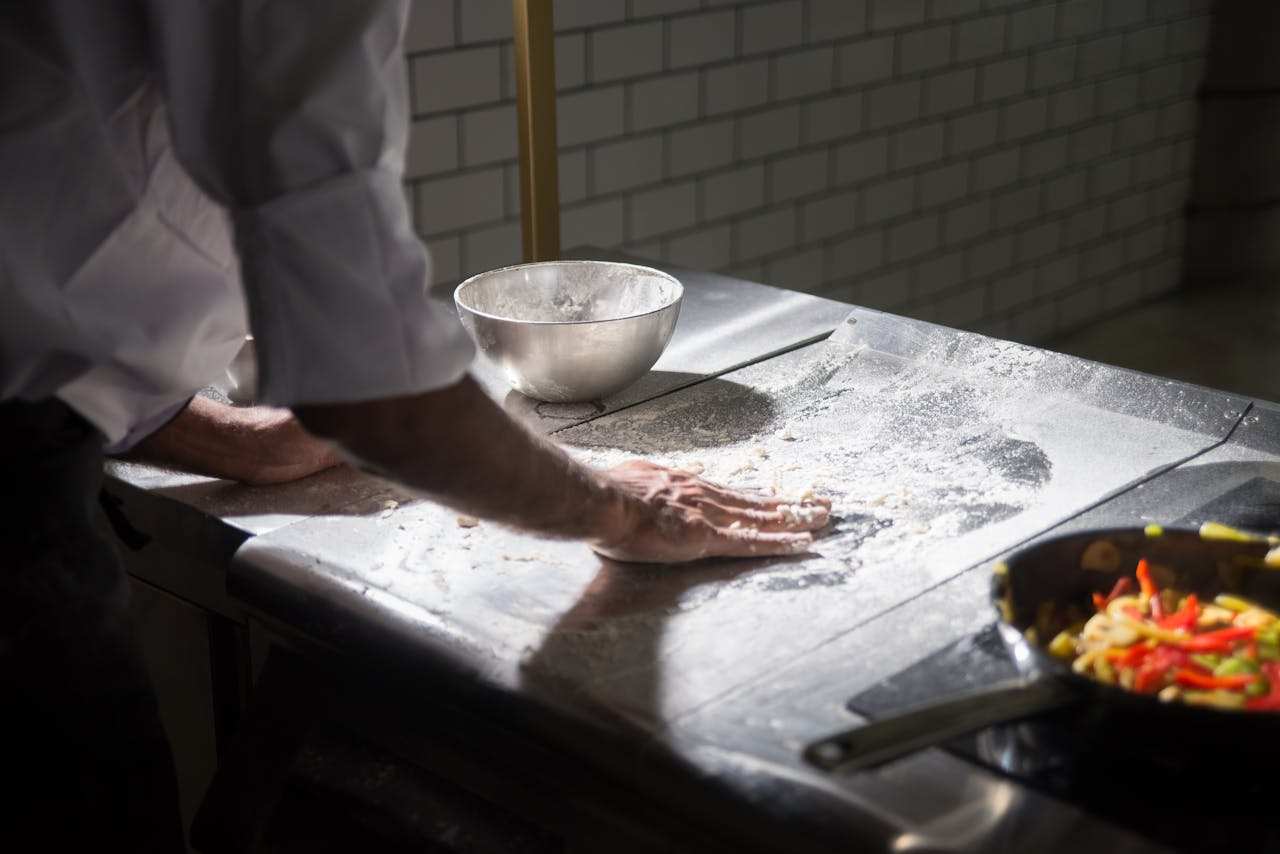 A chef kneads dough in a commercial kitchen setting with a focus on food preparation.